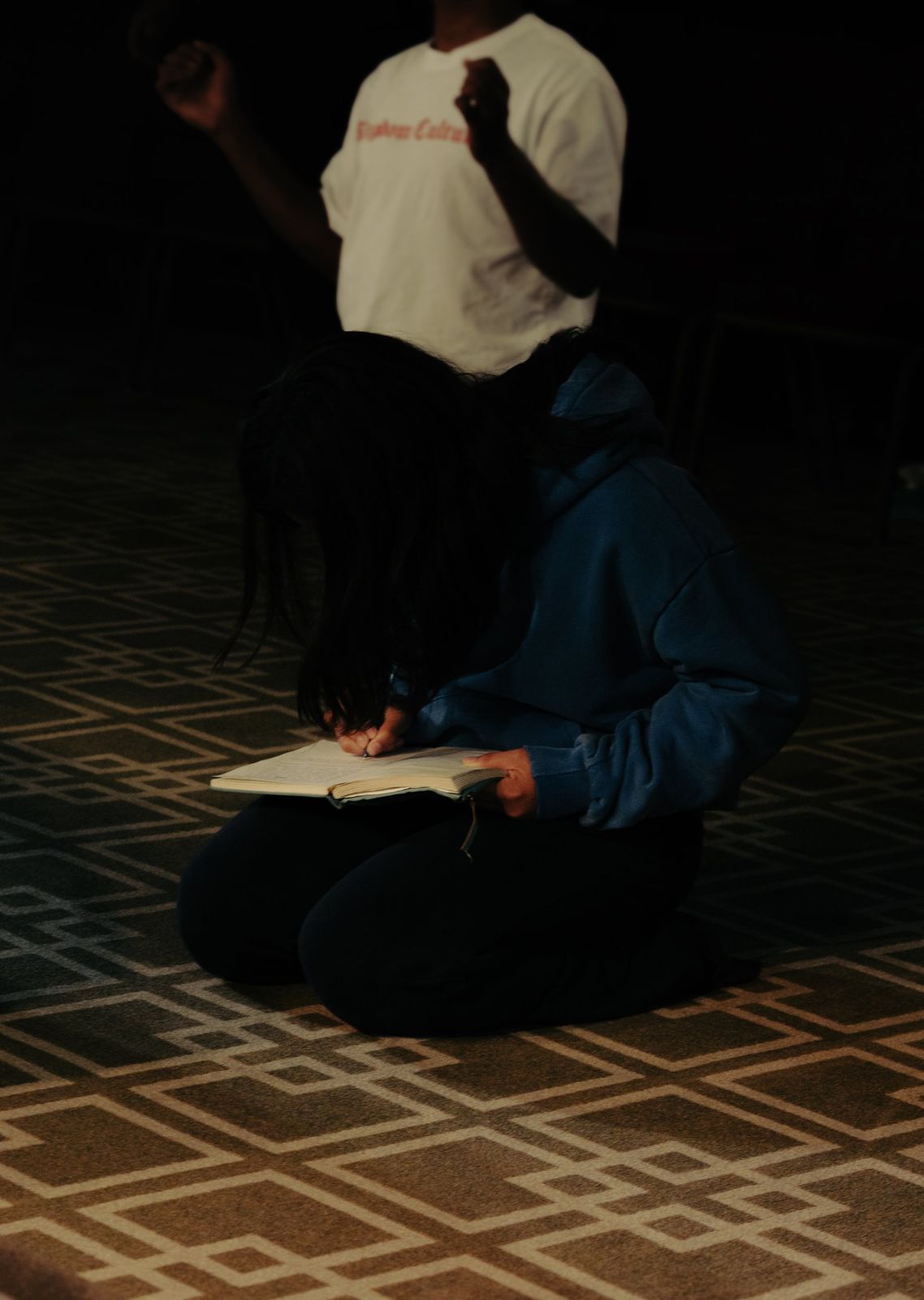 A young woman kneeling on the floor, writing in her journal during worship